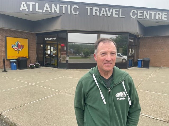 Man in green shirt standing in front of a building with a sign Atlantic Travel Centre