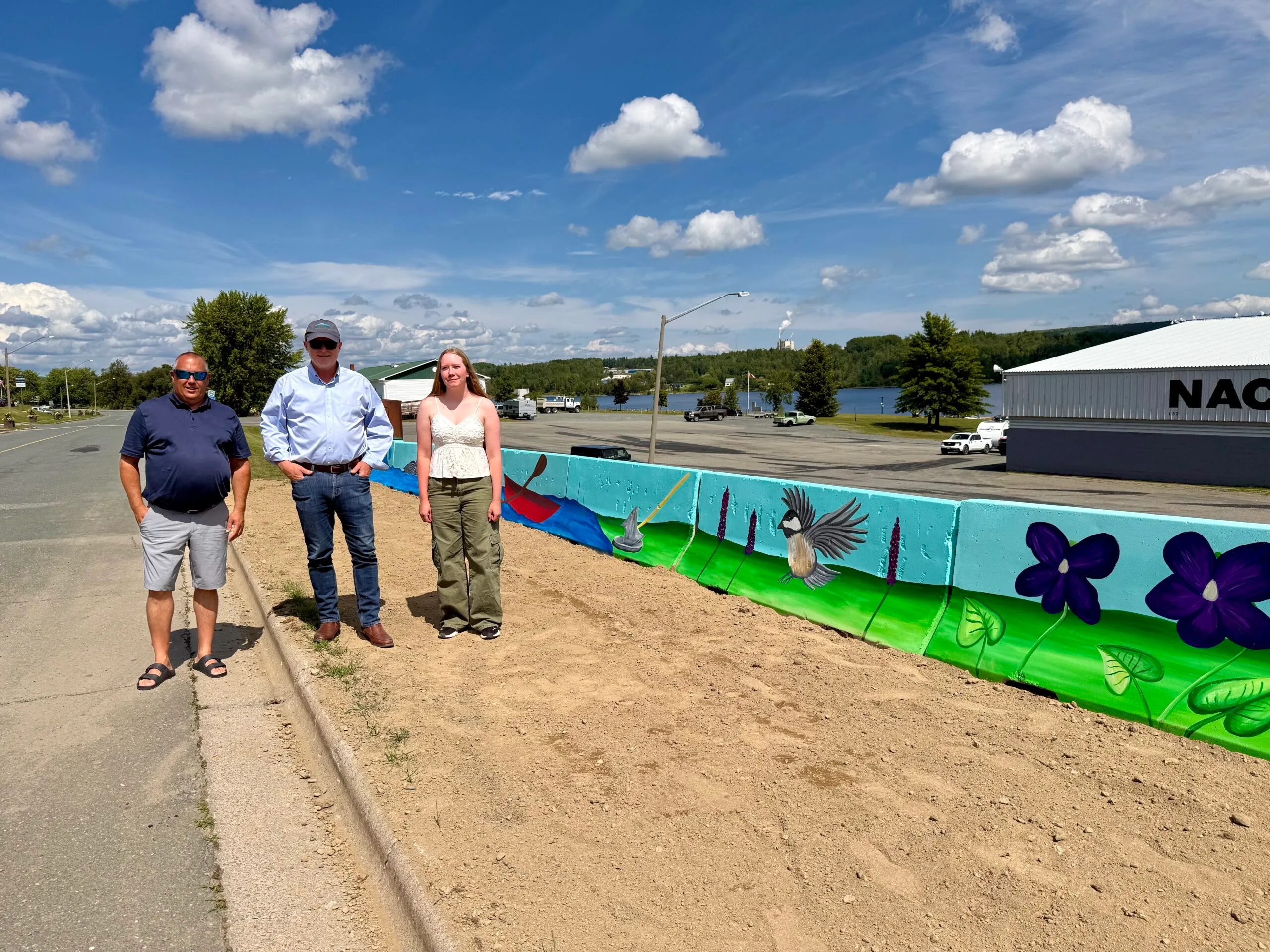 Mayor Tim Fox and Deputy Mayor Greg MacFarlane with Neveah Royal, the Nackawic Marina summer student who has been busy painting a mural at the end of Landegger Drive. Neveah said it has taken her over 60 hours, but she has been enjoying it. She designed the mural herself, incorporating many items representing New Brunswick and the Nackawic-Millville area. (Karen Howell photo)